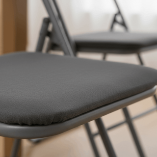 Zoom sur l'assise rembourrée en tissu effet velours gris d'une chaise pliante, montrant la qualité des finitions